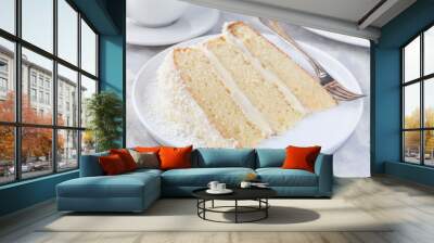 Piece of homemade coconut cake with cream cheese frosting and coconut flakes decoration, on white plate, horizontal Wall mural