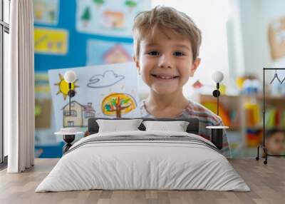 A joyful young boy proudly holding a colorful drawing of a house tree and sun set against a backdrop of a vibrant classroom with educational materials and artwork. Wall mural