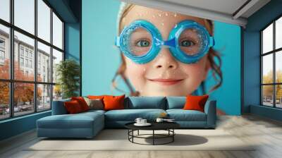 A young girl with sparkling blue eyes wearing blue goggles with water droplets on them smiling against a vibrant blue background. Wall mural