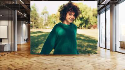 Beautiful young woman smiling posing against nature background with windy curly hair, have positive expression, wearing in green sweater. People, travel and lifestyle. Wall mural