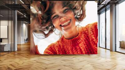 Bottom view of a candid beautiful young woman wearing a knitted orange sweater smiling broadly and looking directly to the camera outdoors. The pretty female has joyful expression, resting in the park Wall mural