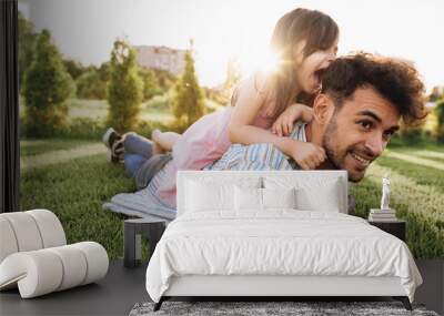 Caucasian happy dad is spending time with his little daughter outdoors. Happy cute little girl playing with her father in the park during the sunset light. Daddy and child sharing love and having fun Wall mural