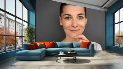 Close-up horizontal shot of cheerful young Caucasian woman with brown hair in bun looking and smiling happily at camera. Brunette female with pretty joyful smile and green eyes posing gray wall.. Wall mural