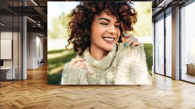 Close-up portrait of beautiful young woman smiling broadly with toothy smile, posing against nature background with curly hair, have positive expression, wearing knitted sweater. People, lifestyle Wall mural