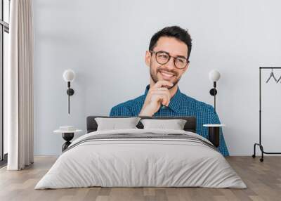 Closeup shot of handsome Caucasian entrepreneur in glasses and blue shirt, looking away with happy smile showing white teeth, holding his chin. People, business and success concept.Advertisement space Wall mural