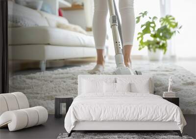 Cropped view of a woman's legs as she vacuums the carpet in a bright, modern living room. Wall mural