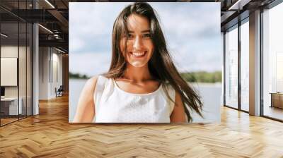 Happy beautiful young woman smiling broadly with healthy toothy smile and with a windy blowing long hair during walking in the park, posing on nature background. Wall mural