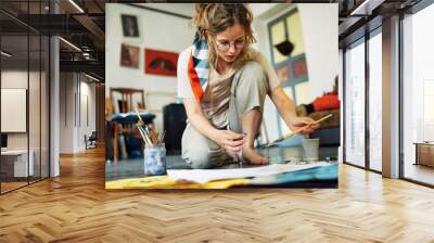 Horizontal image of a pretty female artist sitting on the floor in the art studio and painting on paper with a brush. A woman painter with glasses painting with watercolors in the workshop. Wall mural