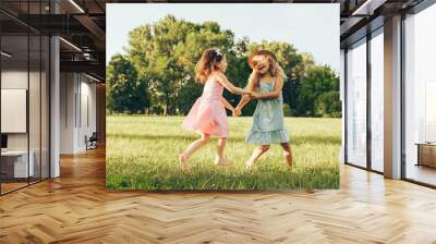 Horizontal image of two little girl dancing on the green grass in the park. Children enjoying summer days in the park. Two sisters having fun on sunlight outdoors. Childhood and friendship concept Wall mural