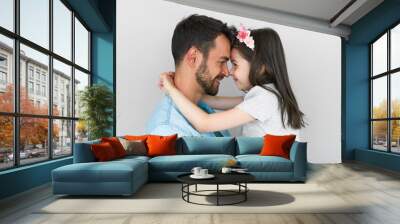 Horizontal studio portrait of happy father smiling, embracing his cute daughter, and looking at each other. Loving daddy and his little girl cuddling and enjoying time together on Father's Day. Wall mural