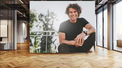 Low view shot of happy stylish young man wears black t-shirt and wirstwatch on the street. Happy smiling man posing for advertisement with copy space, outdoor in the city street. People concept Wall mural