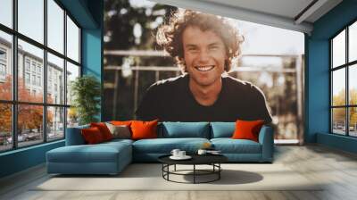 Outdoor closeup portrait of handsome freckled smiling male with curly hair, posing for social advertisement, in the city street on sunset sunlight with copy space for your promotional information Wall mural