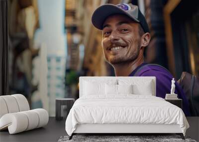 Smiling man in purple shirt and baseball cap standing in urban alleyway with blurred background exuding friendly and approachable demeanor. Wall mural