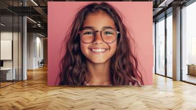 Smiling young girl with glasses and long brown hair against pink background. Wall mural