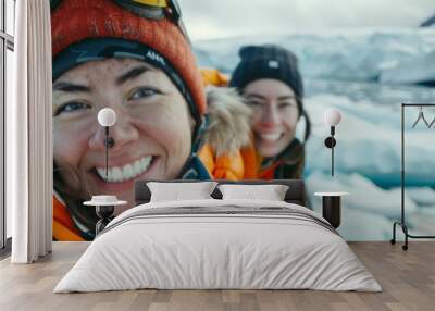 Two women smiling in the snow wearing winter gear with a backdrop of icy terrain. Wall mural