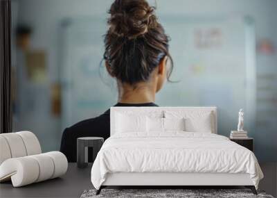 Woman with a messy bun wearing a black blazer standing in an office with a whiteboard in the background. Wall mural