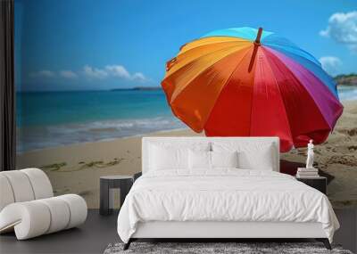 A vibrant beach umbrella stands tall on a sandy beach, with a clear blue sky and calm waves in the background Wall mural