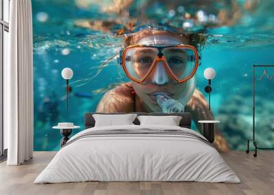 A woman wearing a snorkel mask swims underwater, looking directly at the camera Wall mural