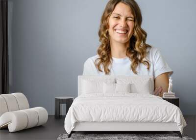 Cheeky woman smiling and winking at camera with confidence, cross arms on chest Wall mural