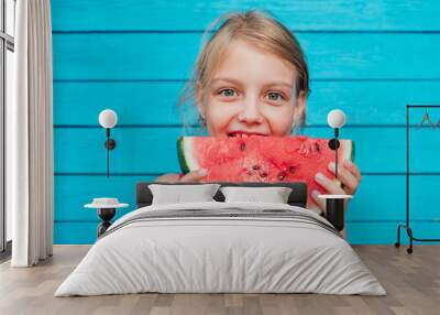 Little girl eating a ripe juicy watermelon over blue plank wall background Wall mural