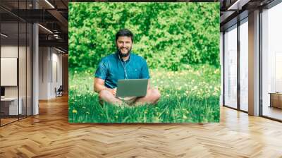 Young businessman or student in casual dress using laptop in the park Wall mural