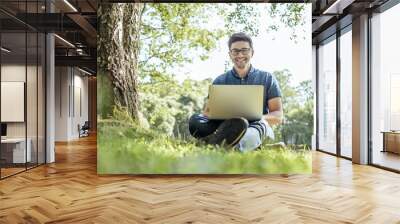 Young man with laptop outdoor sitting on the grass Wall mural