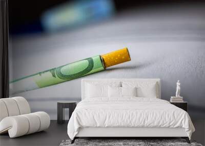 A cigarette butt is on a white surface next to a green bill Wall mural