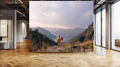 A couple of tourists are embraced standing on top of a mountain in Montenegro. Wall mural