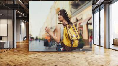 Back view of a young woman traveler with a backpack on her shoulder out sightseeing in a foreign city, stylish female foreigner examines architectural monument during her long-awaited summer vacation Wall mural