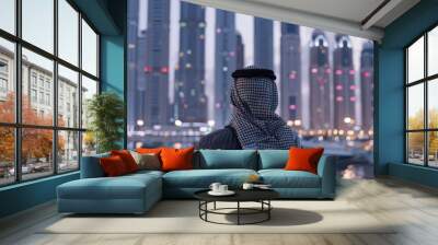 Back view of an Arab entrepreneur or businessman standing against the background of tall skyscrapers or tall buildings at evening time
 Wall mural