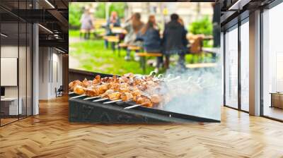 Barbecue fries in the coals. Blurred people eat at the table in the background. Meat and beef at the field kitchen festival. Wall mural