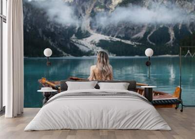 Beautiful girl sitting backwards on a boat on the famous blue lake. Stunning romantic place with typical wooden boats on the alpine lake,(Lago di Braies) Braies lake,Dolomites Wall mural