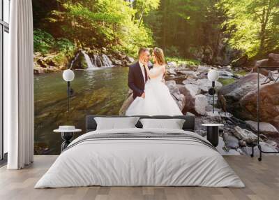 Beautiful newlyweds sit on stones and hug. Stylish wedding recep Wall mural