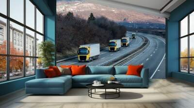 Caravan or convoy of Yellow lorry trucks on country highway under a dramatic sky Wall mural