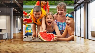 Children eat watermelon on the pier. Children in life jackets rest on the river bank. Camping by the water. Wall mural