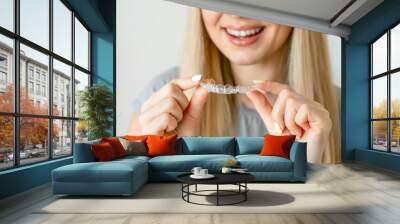 Close up of clear aligners in hands of happy girl who is standing and showing orthodontic device to the camera. Selective focus and isolated background Wall mural