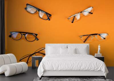 Different types of glasses on an orange background close up. Glasses with rectangular and round frames. Layout for design. Space for text and free space near the object. Wall mural