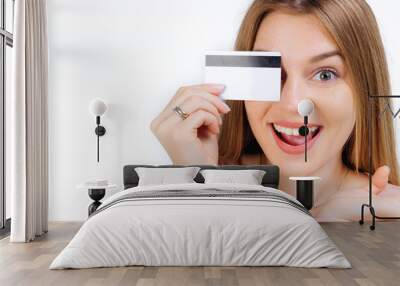 Happy cheerful woman holding a credit card covering one eye. Whi Wall mural