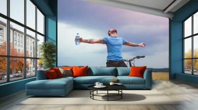 Happy man with bike spreading hands and drinking water resting. Freedom or happiness concept Wall mural