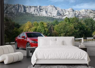 Red car standing on the road near mountains at daytime Wall mural