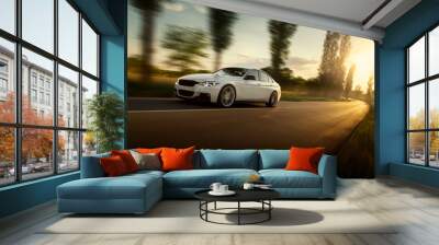 White car is driving on empty countryside asphalt road at sunset Wall mural