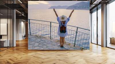 Woman in casual dress and hat with backpack looking to sea. Travel Cinque Terre in Italy in summer sunset Wall mural