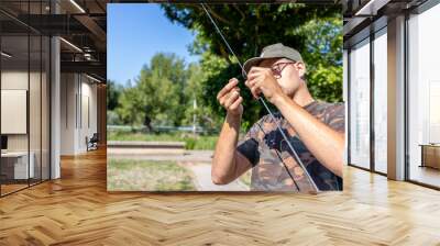 Man tying fishing line to hook in park under clear sky Wall mural