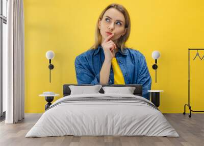 Pensive suspicious attractive woman looking for answers on her questions isolated on yellow background Wall mural