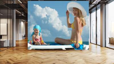 Happy woman in a white hat and the child sit on the beach Wall mural