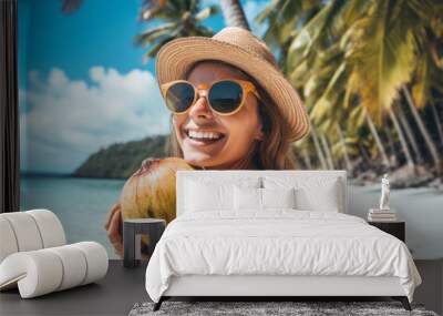 Portrait of young smiling woman in sunglasses and hat holding coconut sitting on exotic beach with palm trees in background, close up view.Theme of exotic and expensive luxury vacation.generative ai Wall mural