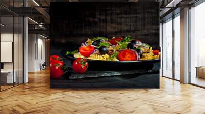 Salad with tomatoes, peppers, olives and pasta. Fresh salad in a black plate on a dark background. Wall mural