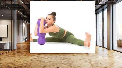 A beautiful young female gymnast with dark long hair stuffed into a bundle in a green sports elastic suit makes a stretch on various muscle groups with sporting inventory Wall mural