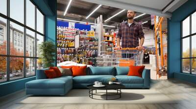 a buyer at a hardware store with a trolley inspects the rows with goods of building materials and tools, the concept of home renovation and housewarming, shopping for renovation Wall mural