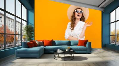 Beautiful caucasian woman in white suit with big hat and sunglasses smiles isolated on orange background Wall mural